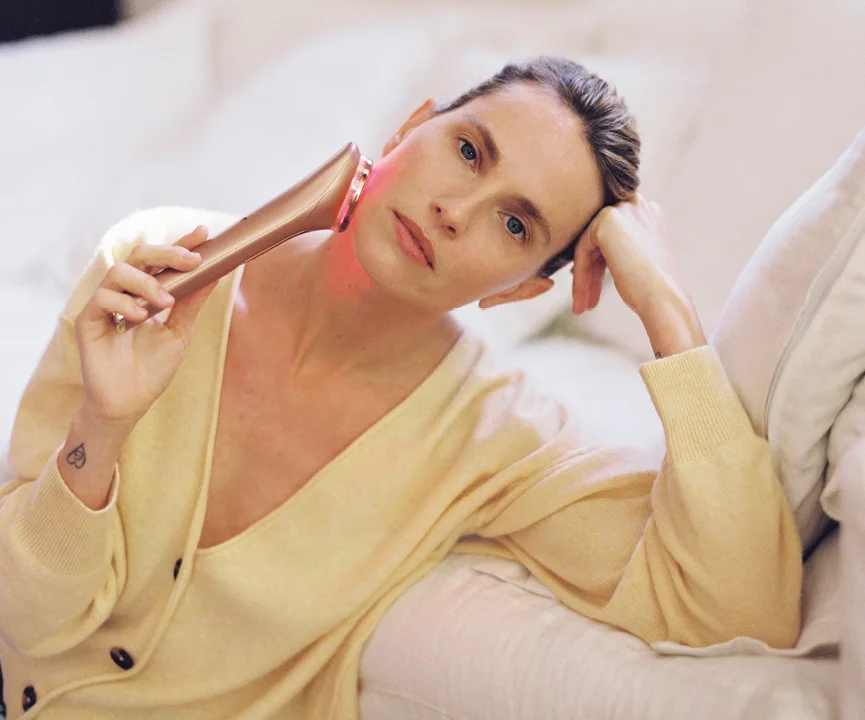 Woman in a pale yellow robe holding a device beside her cheek