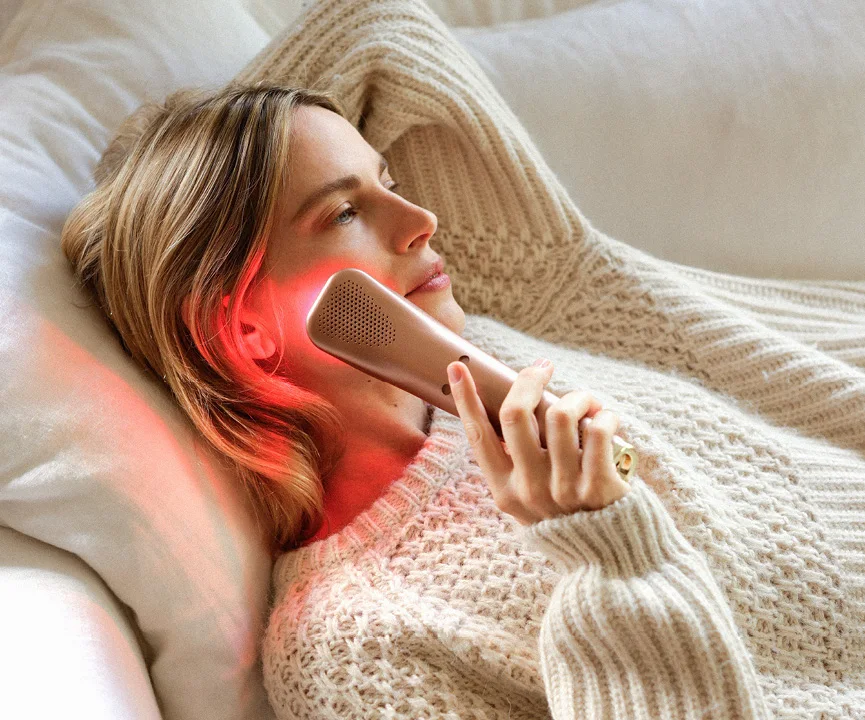 Woman reclining while holding a red-lit device to her cheek